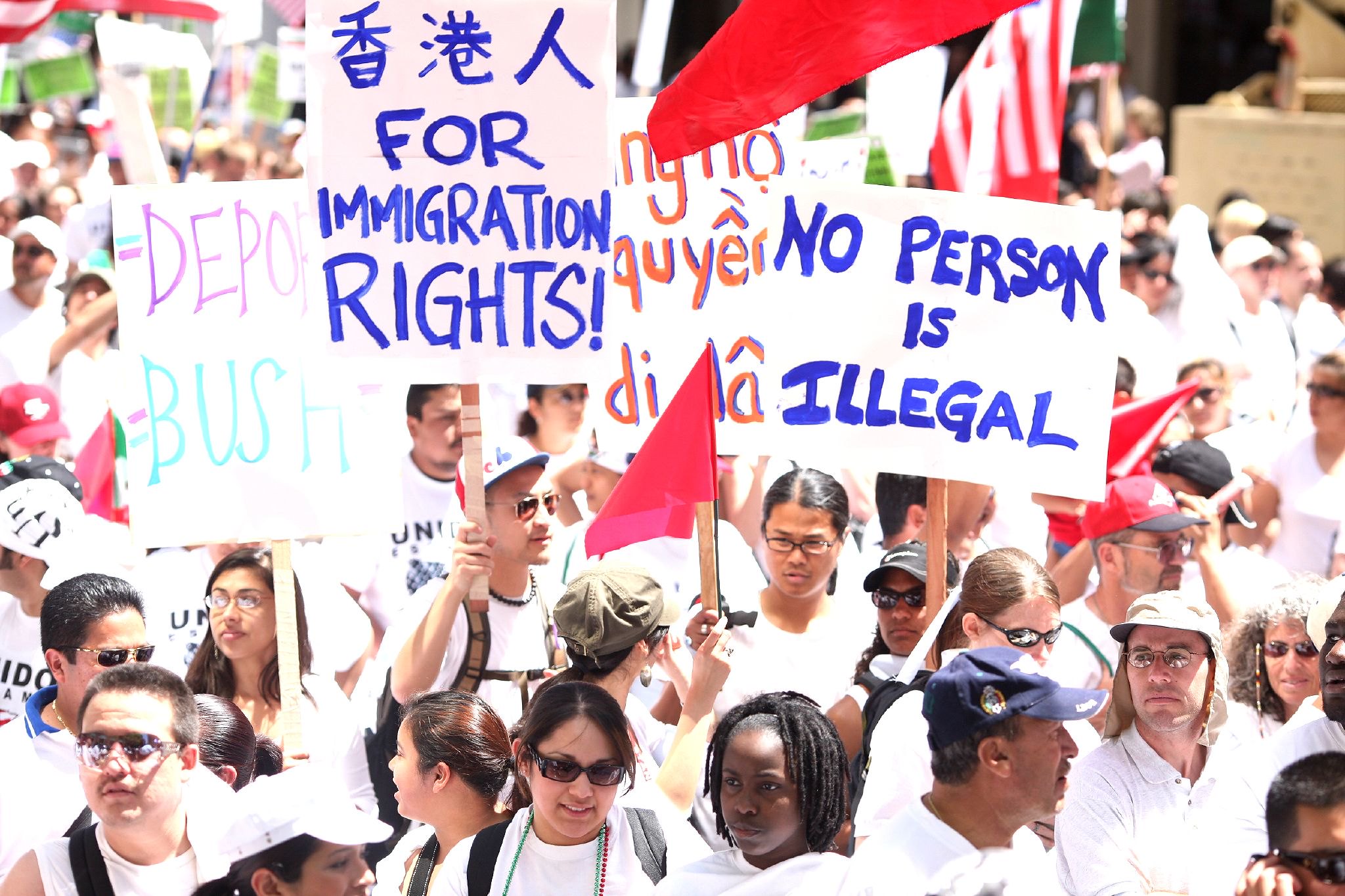 Une foule diversifiée de personnes est entassée par une journée ensoleillée.  Ils tiennent des pancartes lisant "pour les droits d'immigration" et "personne n'est illégal."